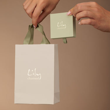 Hands holding a green box and white bag with 'Lily charmed' branding against a brown background