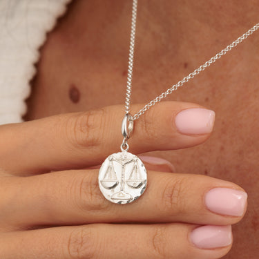 Silver Libra charm necklace with detailed scales motif in hands