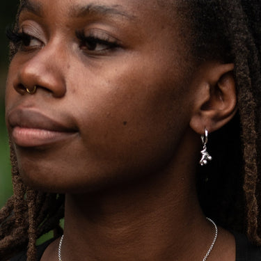 Silver roller skate charm hoop earrings in earlobe piercing on Model